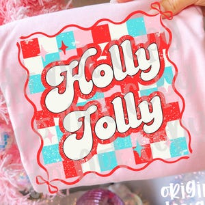 May include: A light pink t-shirt with the words "Holly Jolly" in a retro font. The design features a red and blue checkered pattern with stars. The words are outlined in red and white. The words "original designer" are in the bottom right corner.