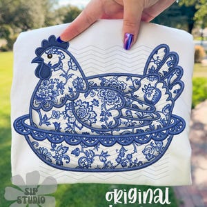 May include: White sweatshirt featuring a blue and white floral design of a hen in a decorative bowl. The design includes the text "original designer" and "SIP STUDIO DO NOT COPY".