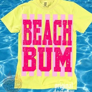 May include: Yellow t-shirt with the words "BEACH BUM" in large, pink, block letters. The text is set against a background of pink and yellow vertical stripes. The shirt has a crew neck and short sleeves.