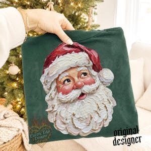 Puede incluir: Una sudadera verde oscuro con un gr&aacute;fico de estilo pintura al &oacute;leo texturizada que representa a Santa Claus. El dise&ntilde;o muestra a un Santa sonriente con un gorro rojo y una espesa barba blanca, realizado con pinceladas visibles y marcadas.