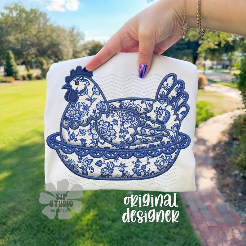 May include: White sweatshirt featuring a blue and white floral design of a hen in a decorative bowl. The design includes the text "original designer" and "SIP STUDIO DO NOT COPY".