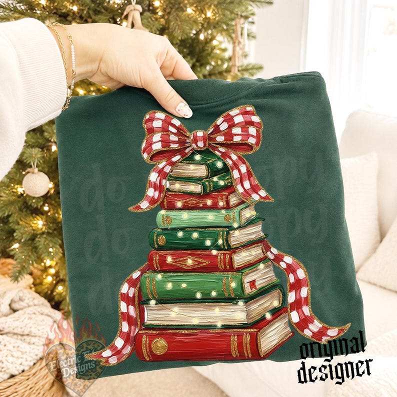 May include: A dark green sweatshirt featuring a graphic of a stack of books arranged in a tree shape, topped with a large red and white checkered bow. The books are decorated with small yellow lights, and the design has a painted texture.