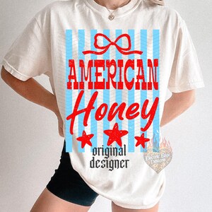 May include: Cream-colored t-shirt with a graphic design featuring the words "AMERICAN Honey" in red, with blue vertical stripes and red stars. The text "original designer" is below the main text.
