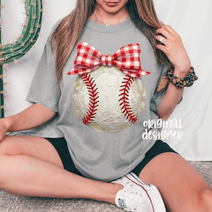 Peut inclure: T-shirt gris avec un motif de baseball et un n&oelig;ud vichy rouge et blanc. La balle de baseball a des coutures rouges et des accents dor&eacute;s. Le texte "original designer" est imprim&eacute; sur le t-shirt.