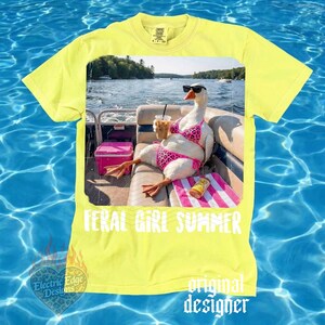 K&ouml;nnte beinhalten: Gelbes T-Shirt mit einer Grafik einer Gans mit Sonnenbrille und pinkem Bikini, die sich mit einem Getr&auml;nk auf einem Boot entspannt. Der Text "FERAL GIRL SUMMER" ist darunter abgebildet. Das Shirt hat auch den Text "original designer".