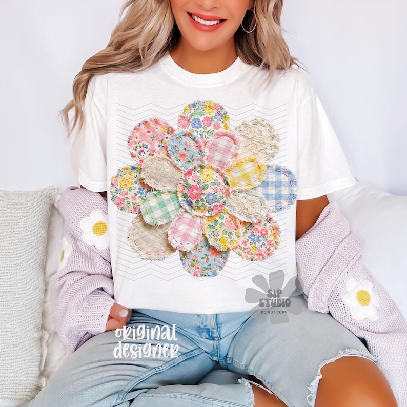 May include: White t-shirt featuring a large, colorful flower design made of fabric patches. The flower has a variety of floral and gingham patterns in shades of pink, blue, yellow, and green. The shirt also has the text "original designer".