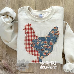May include: Cream-colored sweatshirt featuring a patchwork chicken design. The chicken's body is split, with a red and white gingham pattern on one side and a blue floral pattern on the other. The words "original designer" are printed on the bottom.