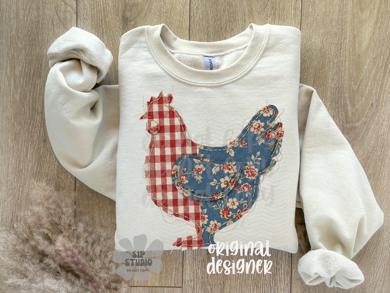 May include: Cream-colored sweatshirt featuring a patchwork chicken design. The chicken's body is split, with a red and white gingham pattern on one side and a blue floral pattern on the other. The words "original designer" are printed on the bottom.