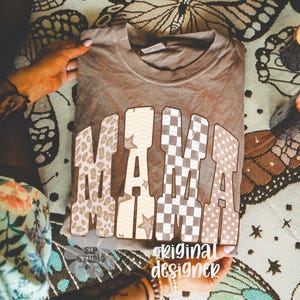 May include: A brown t-shirt with the word "MAMA" in large, patterned letters. The patterns include leopard print, stars, and checkered designs. The text "original designer" is also visible.