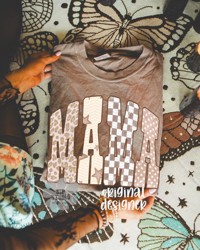 May include: A brown t-shirt with the word "MAMA" in large, patterned letters. The patterns include leopard print, stars, and checkered designs. The text "original designer" is also visible.