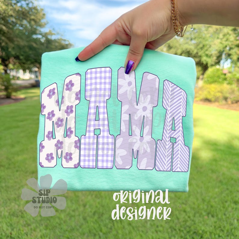 May include: A mint green t-shirt with the word "MAMA" in large, decorative letters. The letters feature floral, gingham, and striped patterns in white and purple. The words "original designer" are printed in white.