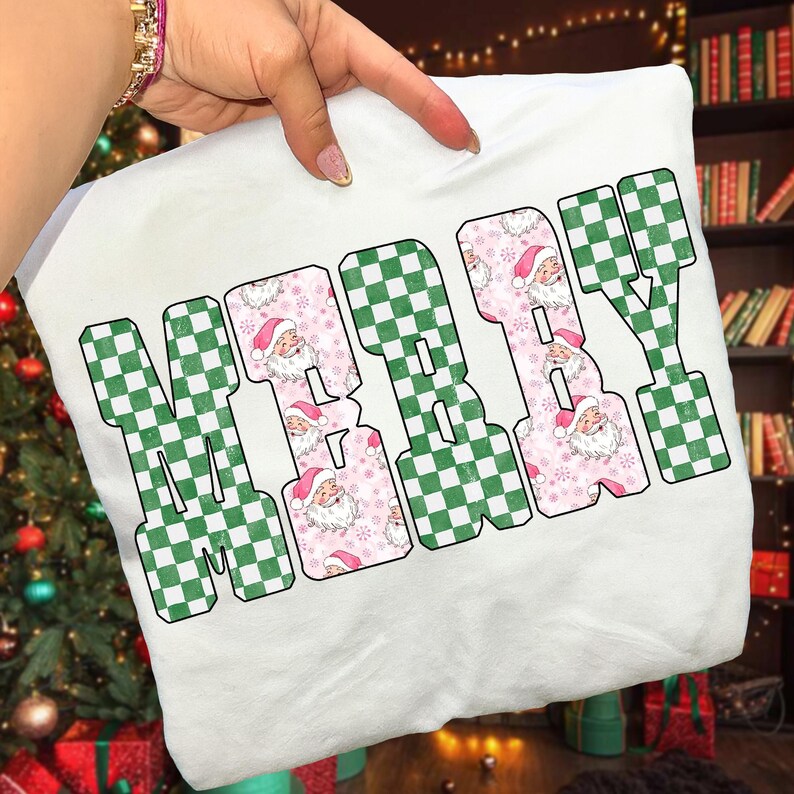 May include: White Christmas-themed sweatshirt with the word "MERRY" in a green checkered pattern and "BABY" in a pink Santa Claus pattern. The Santa Claus pattern includes snowflakes and Santa faces. The sweatshirt is held by a person.