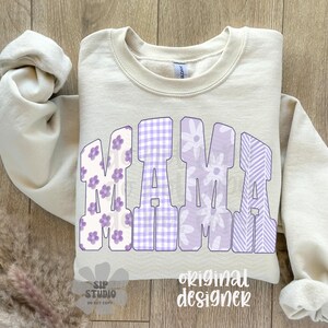 May include: A cream-colored sweatshirt with the word "MAMA" in large, purple letters. The letters have floral, gingham, and striped patterns. The words "SIP STUDIO" and "original designer" are also visible.