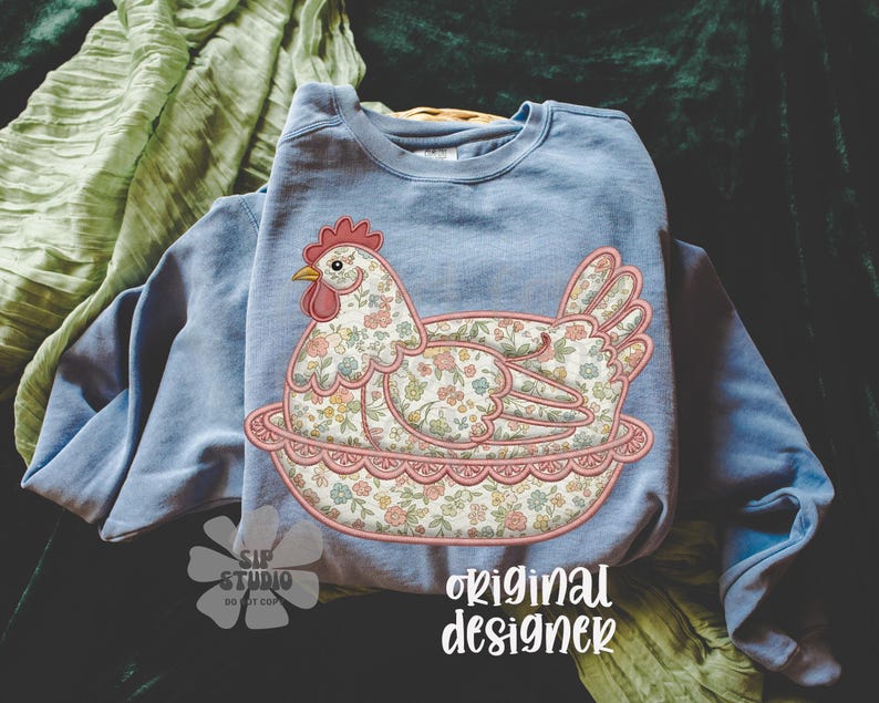 May include: A light blue sweatshirt featuring an embroidered hen design. The hen is adorned with a floral pattern in shades of pink, blue, and yellow. The design includes the text "original designer".