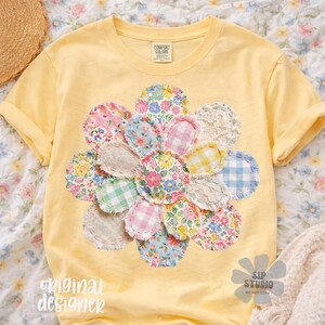 May include: Yellow t-shirt with a large floral design made of various patterned fabric circles. The flower design includes pink, blue, and yellow floral and gingham patterns. The shirt has rolled-up sleeves and the text "original designer" is visible.