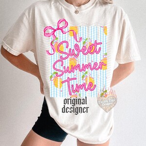 May include: Cream-colored t-shirt with a graphic that says "Sweet Summer Time" in pink script. The design includes a pink bow, lemons, and a blue and white checkered pattern. The words "original designer" are printed below.