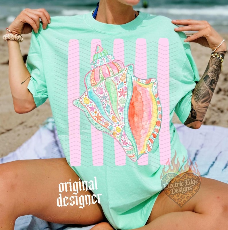 May include: A light green t-shirt featuring a large, colorful seashell design with pink vertical stripes. The seashell is detailed with various sea creatures and vibrant colors. The text "original designer" is visible.