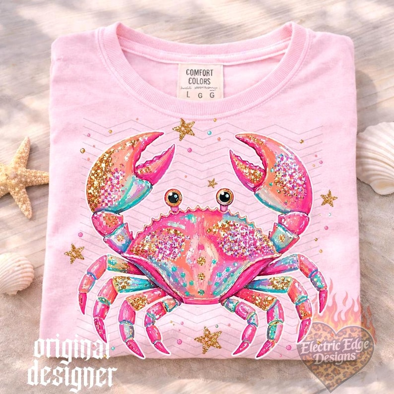 May include: Pink t-shirt featuring a colorful crab design with glitter accents and star details. The crab has pink, orange, and teal hues. The shirt includes the text "original designer" and "Electric Edge Designs".