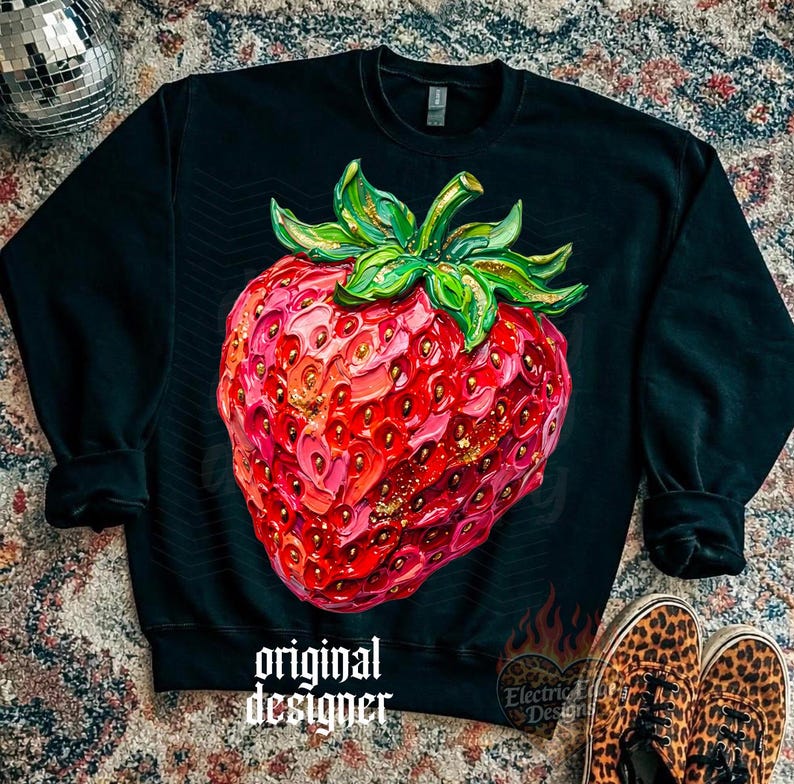 May include: Black sweatshirt featuring a large, detailed strawberry graphic. The strawberry is rendered in shades of red and pink with gold accents and green leaves. The text "original designer" is printed on the bottom.