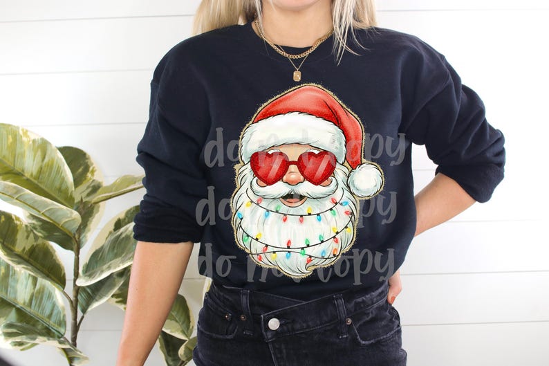 May include: A navy blue sweatshirt featuring a Santa Claus graphic. Santa is wearing heart-shaped sunglasses and a red hat. His beard is adorned with colorful Christmas lights, creating a festive holiday design.