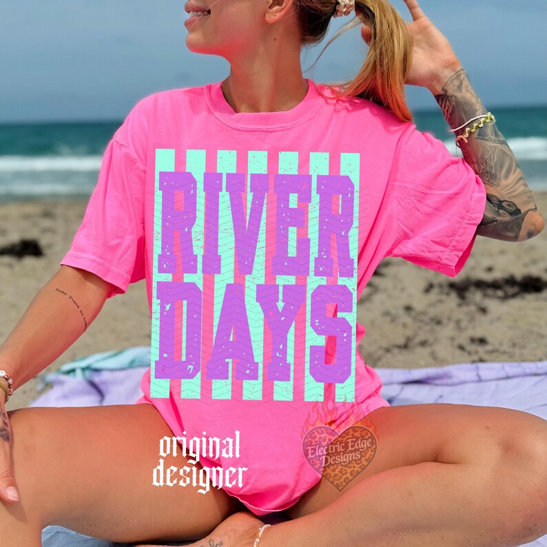 May include: A bright pink t-shirt with the words "RIVER DAYS" in a vertical striped design of light blue and purple. The words "original designer" are printed in a gothic font at the bottom of the shirt.
