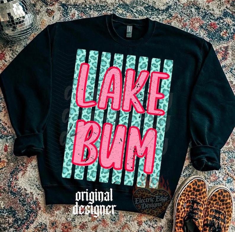 May include: Black sweatshirt with the words "LAKE BUM" in pink, set against a teal leopard print background. The design includes vertical stripes and the words "original designer" at the bottom. Leopard print shoes are visible.