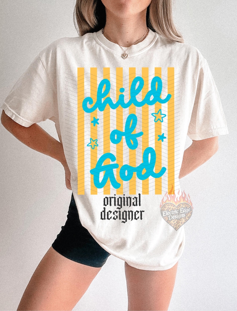 May include: Cream-colored t-shirt with the text "child of God" in turquoise, set against yellow and white vertical stripes. The shirt also features the words "original designer" in black, and a logo.