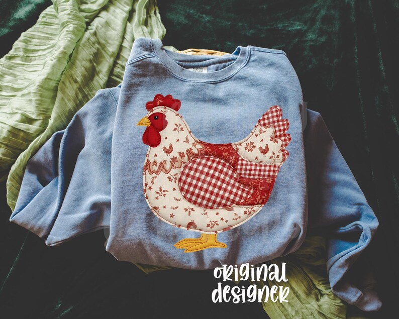 May include: A pale blue sweatshirt with a chicken appliqu&eacute;. The chicken design uses red and white floral and gingham patterns, with a red comb and yellow feet. The text "original designer" is at the bottom of the image.