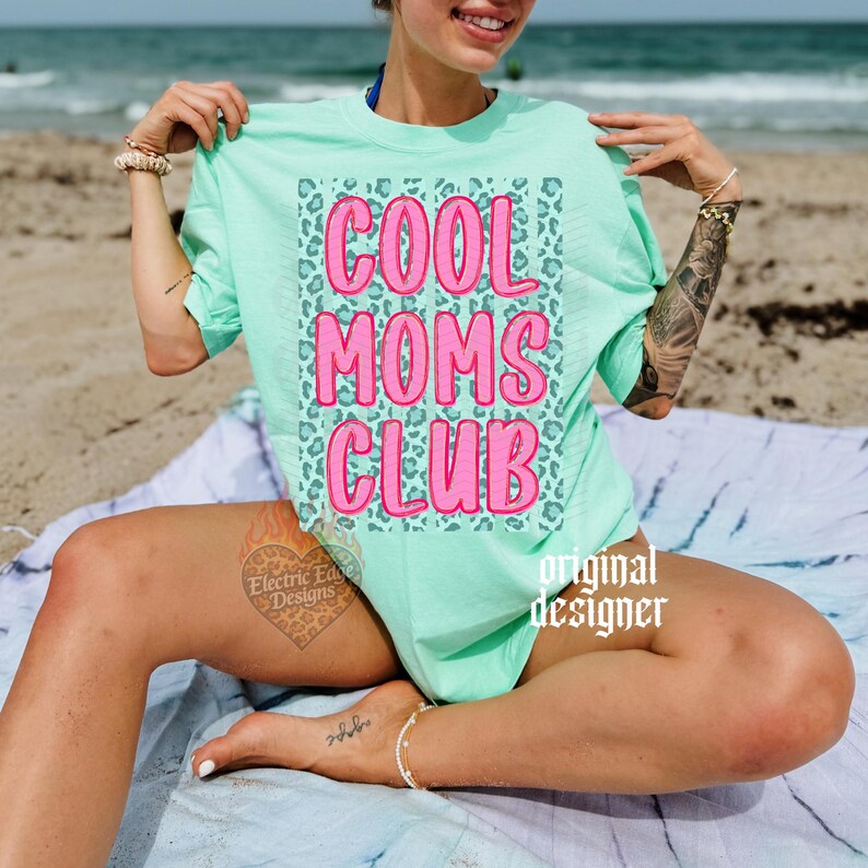 Peut inclure: T-shirt vert clair avec l'inscription "COOL MOMS CLUB" en rose, lettres en forme de bulles. Le texte est plac&eacute; sur un fond &agrave; imprim&eacute; l&eacute;opard. Les mots "original designer" sont imprim&eacute;s en blanc.