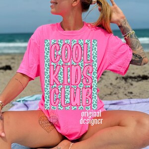 May include: A bright pink t-shirt with the words "COOL KIDS CLUB" in a bubble font. The text is set against a teal leopard print background. The words "original designer" are printed in white below the graphic.