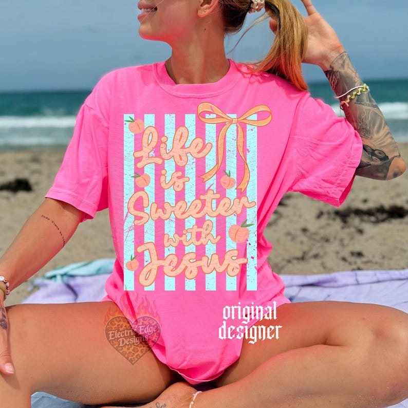 May include: A bright pink t-shirt with the text "Life is Sweeter with Jesus" in a playful font. The design includes peaches and a bow, set against blue and white stripes. The words "original designer" are printed on the bottom right.