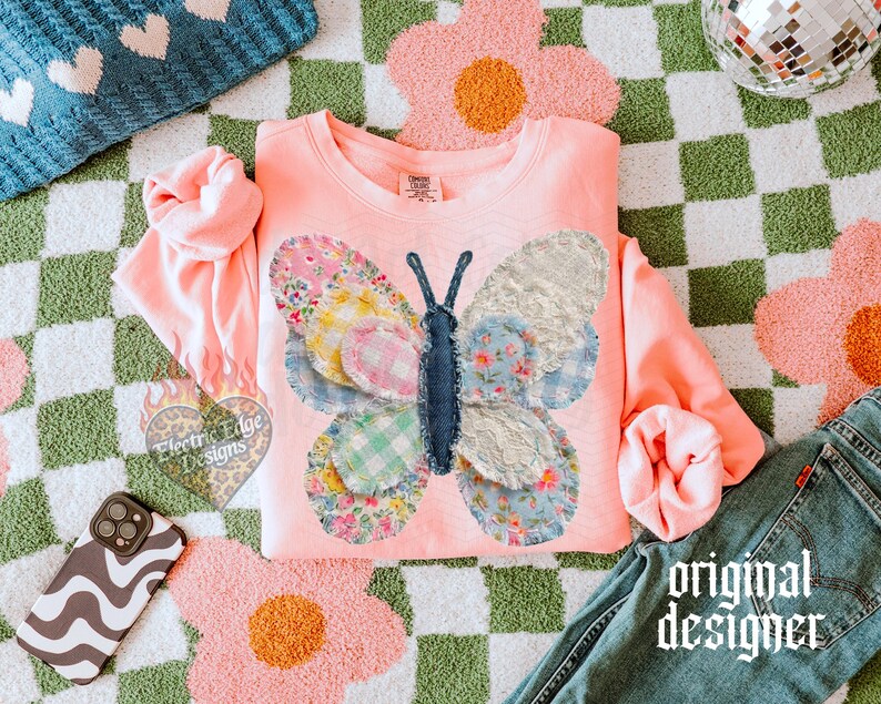 May include: A coral-colored sweatshirt features a patchwork butterfly design with floral and patterned wings. The butterfly is centered on the chest. The words "original designer" are printed on the bottom right of the image.