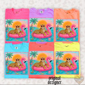 May include: A collection of colorful t-shirts, each featuring a graphic of a leopard wearing sunglasses, lounging on a pink flamingo float in the ocean. The design includes a sunset, palm trees, and the text "original designer".