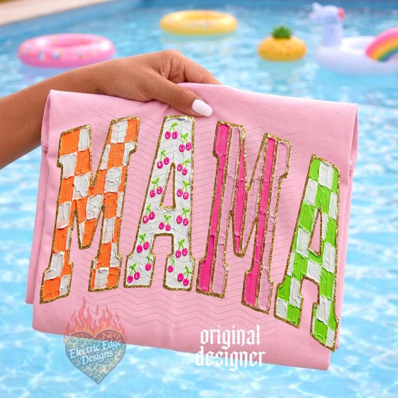 May include: Pink t-shirt with the word "MAMA" in large, colorful letters. The "M" is orange and white checkered, the "A" is white with cherry designs, the second "M" is pink, and the final "A" is green and white checkered. Gold trim outlines the letters.