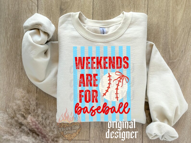 May include: A cream-coloured sweatshirt with the words "WEEKENDS ARE FOR baseball" in red script. The design includes a baseball graphic and light blue vertical stripes. The sweatshirt is a casual style.
