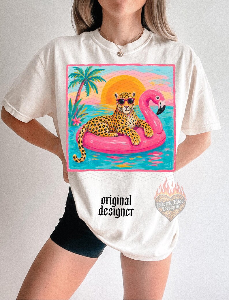 May include: Cream-colored t-shirt featuring a leopard wearing sunglasses, lounging on a pink flamingo float in a tropical scene. The design includes a sunset, palm tree, and the text "original designer".