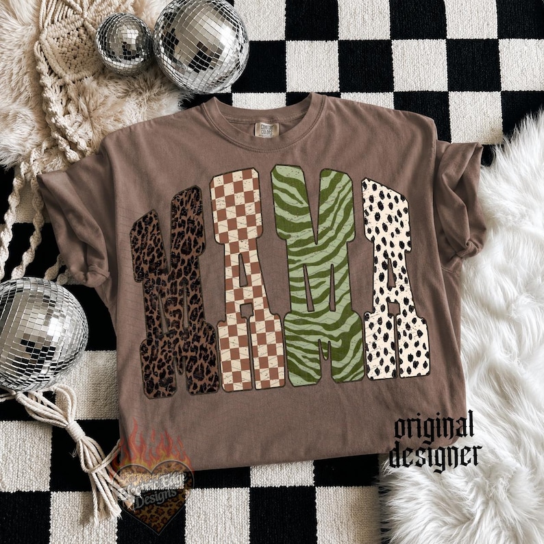 May include: A brown t-shirt featuring the word MAMA in large block letters. Each letter has a distinct pattern: leopard print, brown and white checkerboard, green zebra stripes, and black and white dalmatian spots. The text original designer is visible.