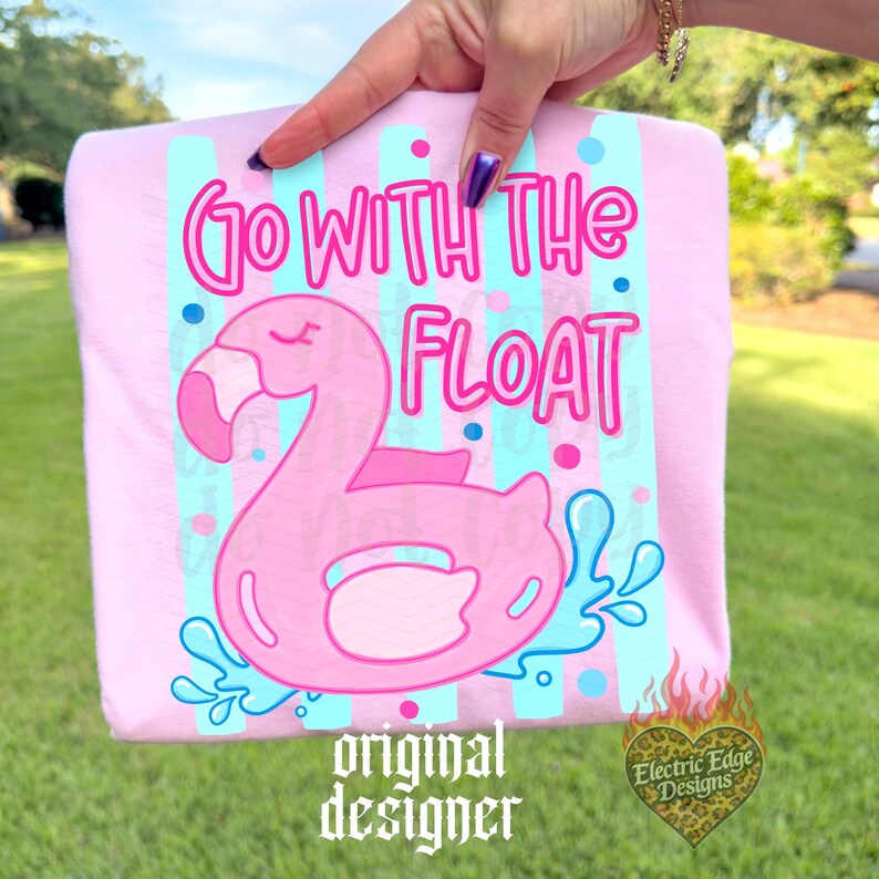 May include: A light pink t-shirt featuring a pink flamingo float with the text "Go With The Float". The design includes blue and pink accents, and the words "original designer" are at the bottom.
