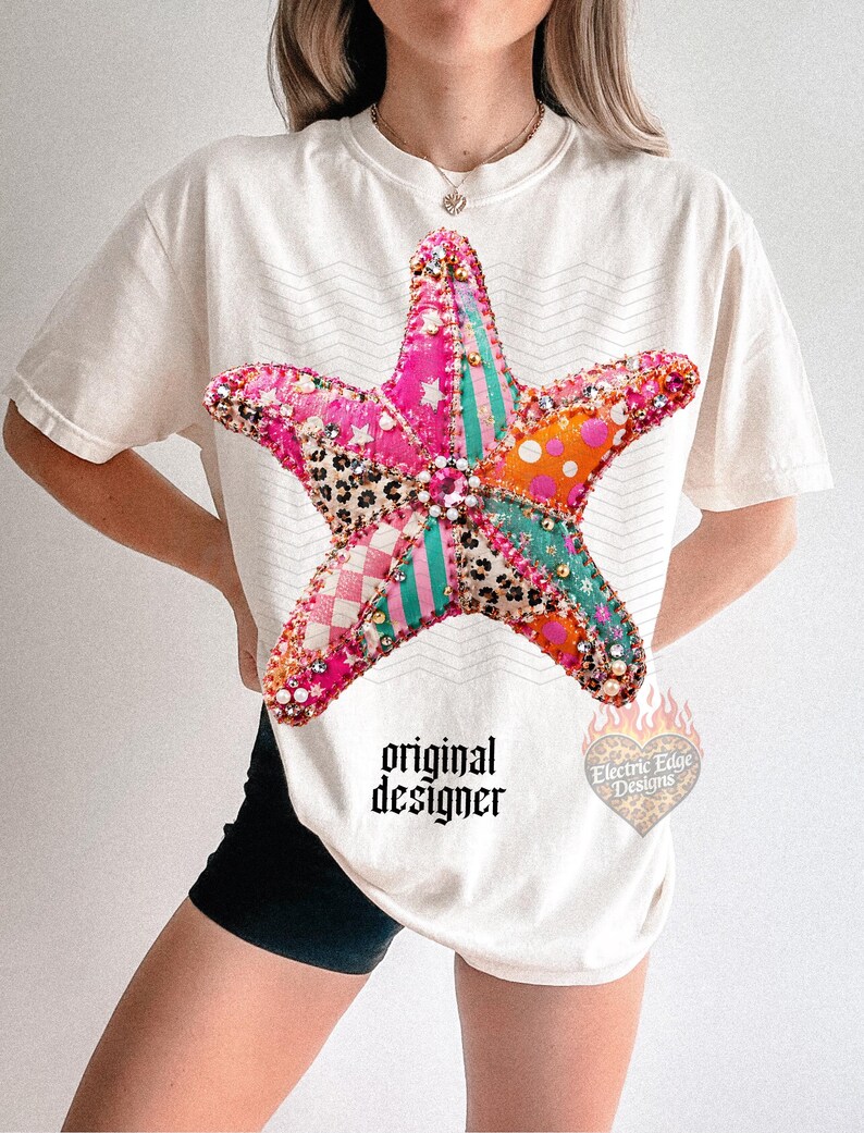May include: Cream-colored t-shirt featuring a large, colorful starfish design. The starfish is made of various patterned fabrics and embellished with beads. The text "original designer" is printed below the starfish.