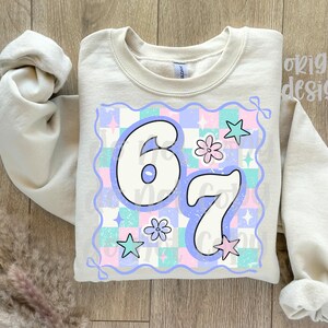 May include: A beige sweatshirt with the number "67" in a retro font, set against a pastel checkered background with stars and flowers. The words "original designer" are printed on the top right.