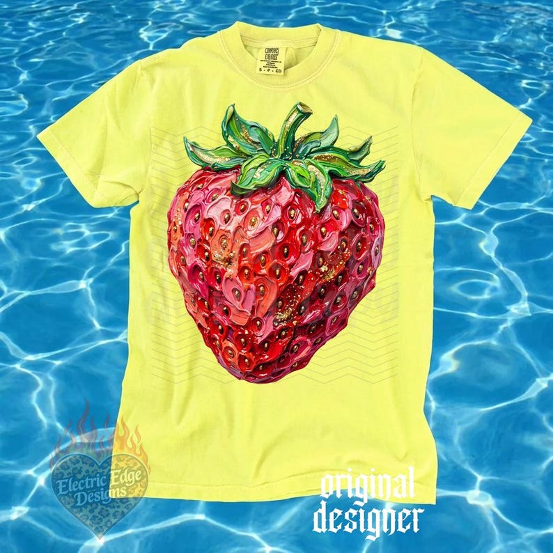May include: A yellow t-shirt featuring a large, detailed illustration of a ripe strawberry. The strawberry is predominantly red with pink and gold accents, and green leaves. The shirt has the text "original designer" and "Electric Edge Designs".