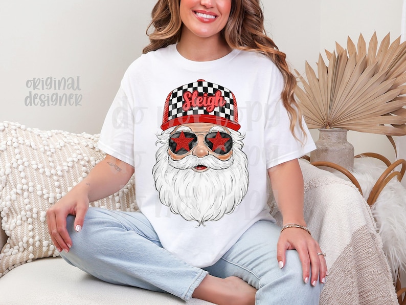 May include: White t-shirt featuring a Santa Claus graphic. Santa wears a red and black checkered hat with the word "Sleigh" and star-shaped sunglasses. The design has a festive, holiday theme.