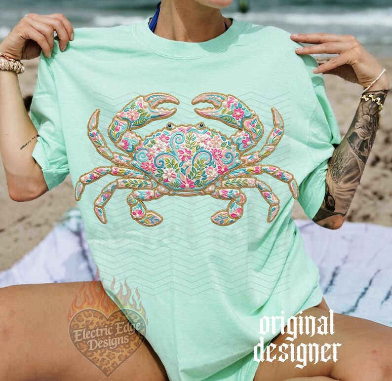 K&ouml;nnte beinhalten: Hellgr&uuml;nes T-Shirt mit detailliertem Krabben-Design. Die Krabbe ist mit einem Blumenmuster in Rosa, Blau und Gold verziert. Das T-Shirt hat kurze &Auml;rmel und eine lockere Passform, ideal f&uuml;r einen Tag am Strand.