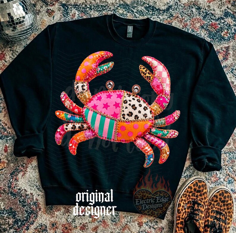 May include: Black sweatshirt featuring a colorful crab design with patchwork patterns. The crab has pink, orange, and green sections with star, leopard, and striped patterns. The text "original designer" is at the bottom.