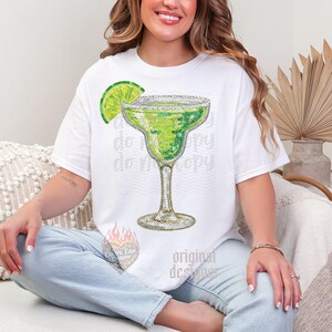 May include: White t-shirt featuring a sparkling margarita design with a lime wedge. The margarita glass is embellished with rhinestones. The words "do copy" are faintly printed on the shirt. The design is by "Original Designer".