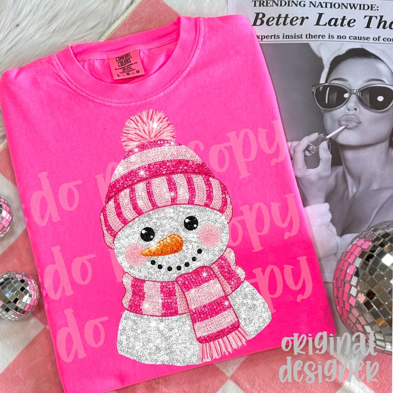 May include: A vibrant pink Comfort Colors sweatshirt with a glittery snowman design. The snowman has a pink and white striped hat and scarf, a carrot nose, and black eyes. The text "do copy" is printed on the shirt.