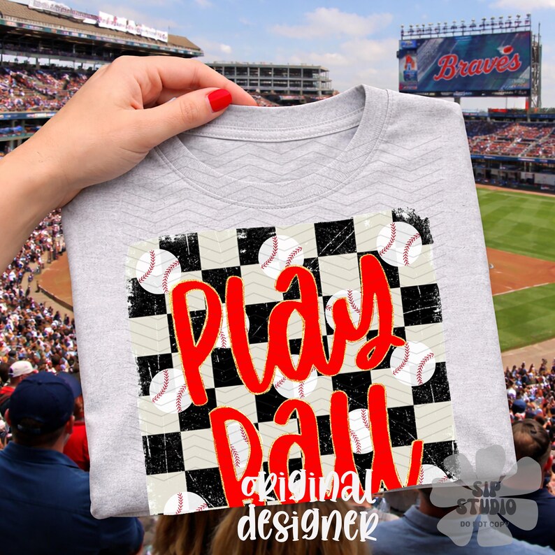 May include: A light gray t-shirt featuring a baseball-themed design. The design includes a checkered pattern with baseballs and the words "Play Ball" in red script. The words "original designer" are also printed on the shirt.