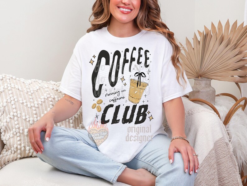 May include: White t-shirt with the words "COFFEE CLUB" in a bold, black font, with the phrase "running on caffeine" below. A graphic of a coffee cup and coffee beans are also featured. The shirt is a casual, everyday wear item.