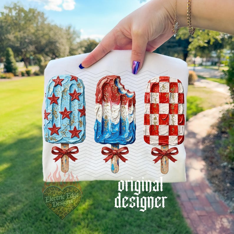 Comfort Colors Mockup. May include: White t-shirt featuring three popsicle designs in red, white, and blue. One popsicle is blue with red stars, another is red, white, and blue with a bite taken out, and the last is red and white checkered. Each has a wooden stick and a red bow.