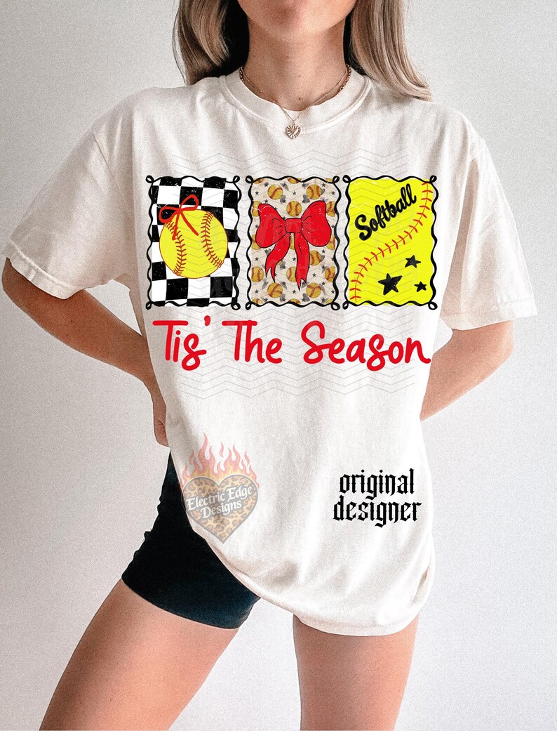 May include: An off-white t-shirt featuring three rectangular graphics with a softball, a red bow, and the word Softball. Below, the red text reads Tis' The Season. A small heart-shaped logo with flames and the text Electric Edge Designs is visible.
